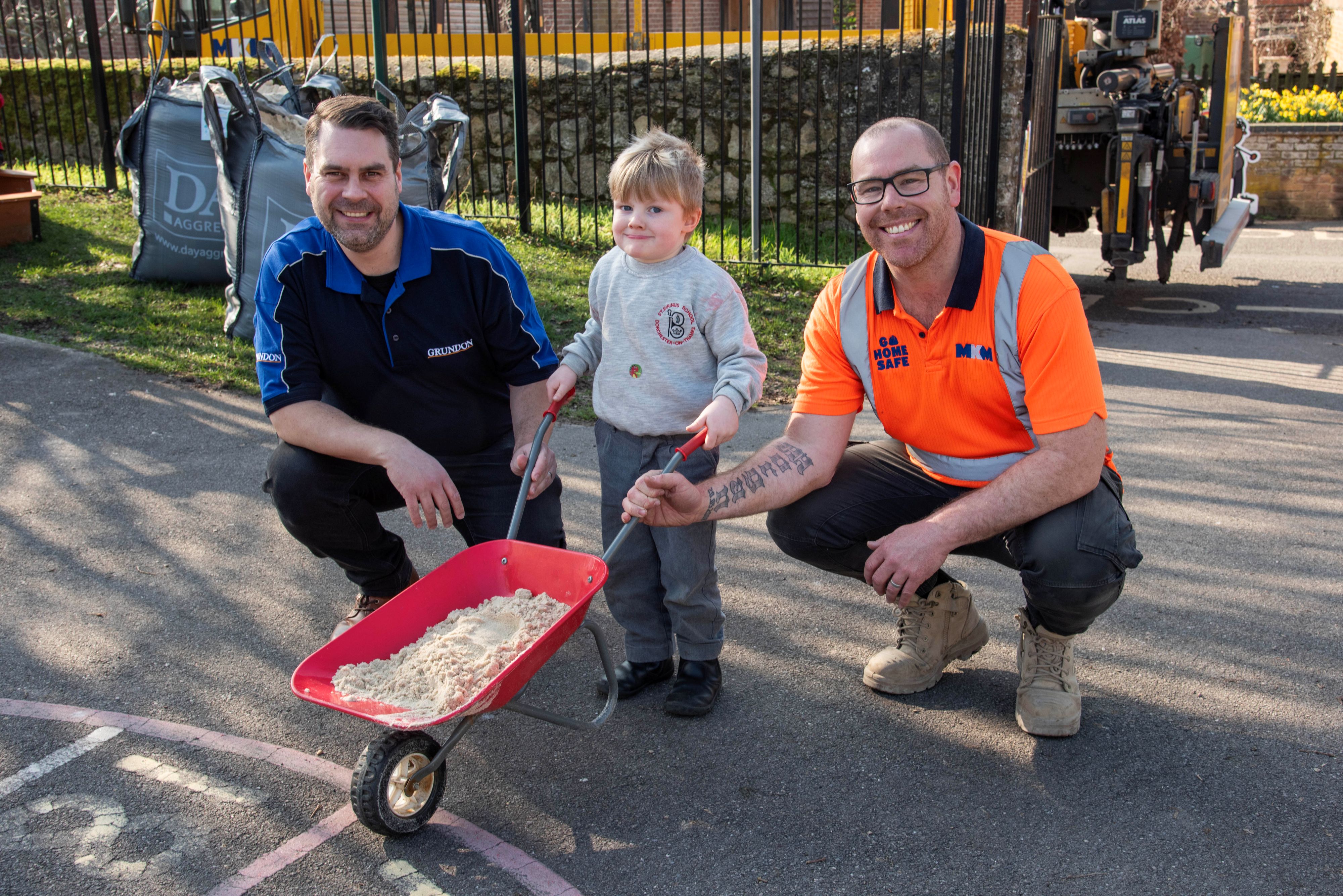 Chris Cowper from Grundon (left) and Dean Evans from MKM Building Supplies (right) with a pupil helping wheelbarrow the sand to the new sandpit.